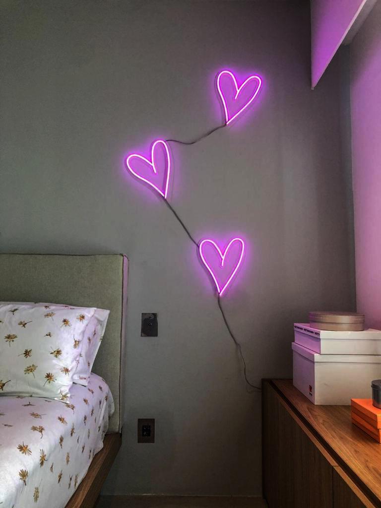 Quarto com três corações em neon roxo acima da cama