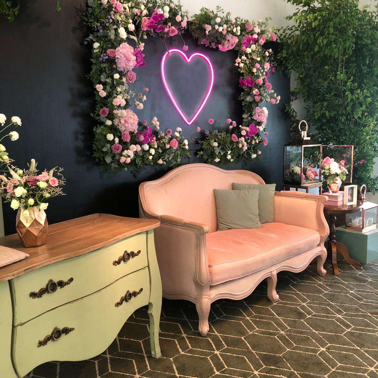 Coração em neon rosa em painel de flores com sofá