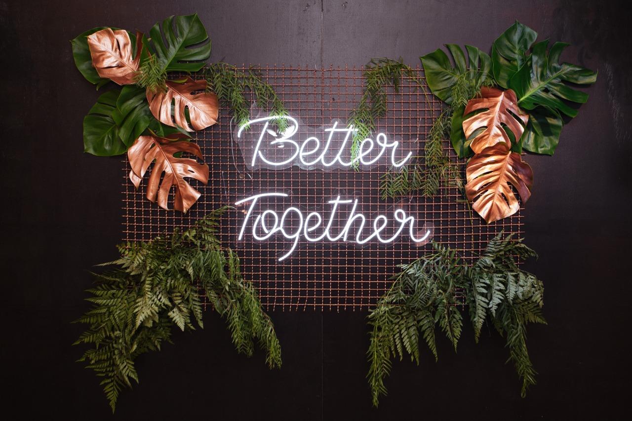 Neon branco Better together em parede com folhagens