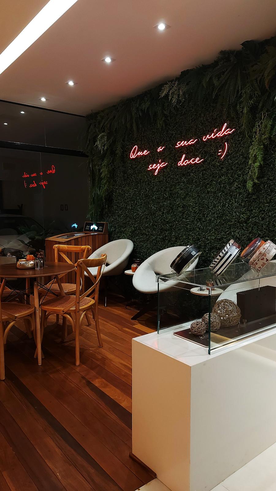 Café com neon cursivo vermelho em jardim vertical e mesas de madeira
